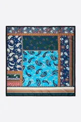 Pañuelo cuadrado con diseño patchwork que combina estampados de paisley, flores y rayas en tonos azules, celestes y verdes. Presenta un borde negro y detalles decorativos en los márgenes.