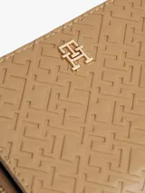 Billetera pequeña de color beige con cierre de cremallera perimetral y un patrón grabado de monograma TH en relieve. Presenta una insignia metálica con el logo TH en el frente.