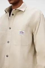 Camisa de H&M confeccionada en pana de algodón, con cuello inglés, cierre frontal con botones a presión y dos bolsillos de parche en el pecho. Presenta mangas largas con puños abotonados y un bajo redondeado, con un corte oversized.