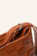 Cartera tipo morral de cuero color beige, con diseño trenzado artesanal, correa larga regulable y cierre superior.
