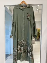 Vestido midi verde militar de corte camisero, con cierre frontal de botones, mangas largas y bolsillos superiores. Presenta un estampado floral artístico en el bolsillo del pecho, el cuello y el ruedo inferior.