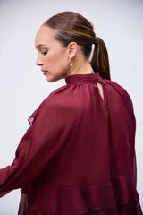 Blusa color bordó con cuello alto, mangas largas acampanadas y detalles de volados en el pecho y el ruedo.