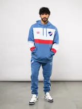 Canguro con capucha de Umbro del Club Nacional de Football, con diseño de bloques de color en azul, blanco y rojo. Presenta bolsillo frontal tipo canguro, cordones ajustables en la capucha y logos bordados del club y la marca.