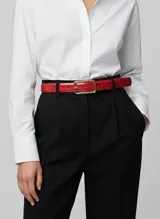 Cinturón fino de color rojo vibrante con textura de cocodrilo y hebilla rectangular metálica en tono dorado claro.