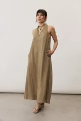 Vestido largo color marrón, sin mangas y con escote halter. Cuenta con bolsillos laterales y corte holgado.