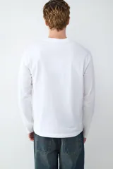 Camiseta de manga larga color blanco, con cuello redondo y corte holgado. Presenta un estampado tipográfico en el pecho y detalles gráficos en la manga.