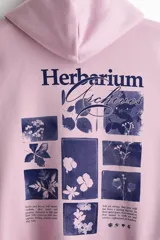 Canguro de algodón con capucha y cordones ajustables, diseño de hombros caídos y bolsillo frontal tipo canguro. Presenta un estampado gráfico en el pecho y puños acanalados.