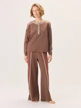 Pantalón de corte ancho y estilo comfy, confeccionado en algodón color marrón. Presenta detalles de franjas verticales en tonos beige y rojo a lo largo de las piernas, con cintura elástica.