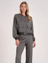 Camperita tipo bomber color beige claro, con cuello redondo acanalado, cierre frontal con broches metálicos y bolsillos delanteros con tapa. Los puños y el bajo son acanalados.