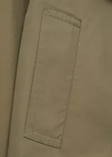 Chaqueta corta de estilo trench con cuello de solapa y cierre frontal de doble botonadura. Presenta diseño recto, manga larga y bolsillos laterales, confeccionada en tejido de mezcla de algodón con forro interior.