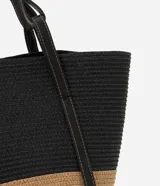 Bolso de playa grande de paja bicolor, negro en la parte superior y beige en la inferior, con asas de cuero sintético negro.
