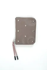 Billetera de cuero sintético color marrón topo, con cierre de cremallera y tirador de cordón rosado con punteras negras. Está decorada con tachas metálicas plateadas en forma de corazón distribuidas en el frente.
