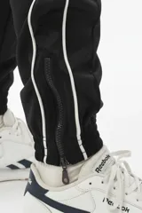 Pantalón de jogging negro con vivo lateral doble blanco, corte holgado, tiro medio, botamanga elastizada y cierres en los tobillos.