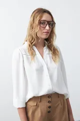 Camisa negra de corte clásico con escote en V, botones frontales y mangas largas con puños. Presenta detalles de recortes calados en la zona de los hombros.