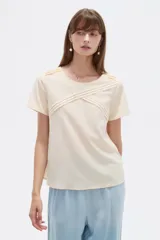 Blusa de viscosa color natural, con cuello a la base, manga corta y detalle de plisado cruzado en el frente. Presenta un corte holgado.