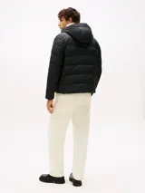 Campera acolchada de color negro confeccionada en tejido ripstop de nailon con acabado repelente al agua. Presenta un diseño con relleno térmico, capucha fija ajustable con cordón, cierre frontal de cremallera y bolsillos laterales con cierre. Incluye el logo de Tommy Hilfiger bordado en el pecho.