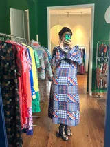 Vestido largo de crepe estampado con diseño patchwork en tonos azules, rojos y blancos. Tiene cuello redondo, mangas largas acampanadas y corte recto.