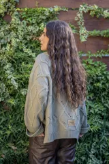 Saco tejido de punto con diseño de ochos y trenzas, color verde oliva. Presenta silueta oversize, cuello camisero, mangas holgadas y botones tipo joya en el frente.