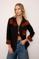 Sobrecamisa de gamuza color marrón con apliques de cuero metalizado en tono cobre en los hombros y bolsillo frontal. Presenta detalles bordados en las mangas, el bolsillo y la espalda, con un diseño de corte recto y cuello camisero.