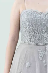 Vestido largo de fiesta color visón, con escote palabra de honor, corsé armado de encaje bordado con apliques florales y falda amplia de tul con volados irregulares.
