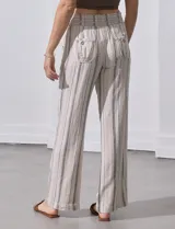 Pantalón largo de lino color beige con rayas verticales marrones. Tiene pretina ancha en punto smock con lazo ajustable, bolsillos verticales delanteros y bolsillos aplicados traseros.