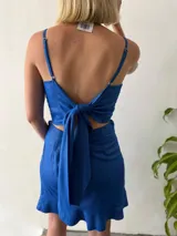Conjunto de dos piezas en lino con lurex color azul brillante. Incluye una falda corta cruzada con volados y un top halter con escote recto y lazo ajustable en el contorno.