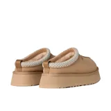 Zuecos UGG modelo Tazz de gamuza color beige, con plataforma alta y detalle de costura trenzada en el borde superior. Presenta el logo de la marca grabado en el lateral.