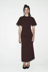 Vestido largo color marrón oscuro, con cuello redondo, manga corta y detalle de drapeado fruncido en el lateral izquierdo, terminando en línea evasé.