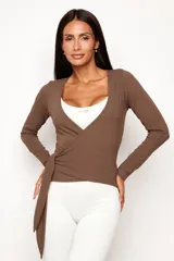 Remera cruzada de manga larga, confeccionada en tejido de viscosa con elastano. Presenta un diseño envolvente con lazo lateral para ajustar en la cintura y escote en V profundo.