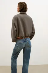 Chaqueta de corte corto y diseño abullonado en color marrón oscuro, con cuello solapa, mangas largas con puños elásticos y cierre frontal con cremallera metálica. Cuenta con bolsillos delanteros de doble vivo.