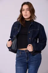 Campera de jean de mujer, color azul claro lavado, con corte cropped y estilo clásico. Presenta cuello camisero, botones metálicos frontales y bolsillos de parche en el pecho.