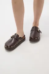 Suecos negros de estilo casual con acabado en eco cuero, detalle de hebilla metálica ajustable en el empeine y tachas decorativas en el contorno de la suela. Presentan una base de corcho y suela de goma dentada.