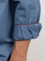 Camisa de hombre color azul, con cuello buttondown, cierre frontal con botones y logo bordado en el pecho. Presenta un acabado vintage logrado mediante el proceso de teñido en prenda.