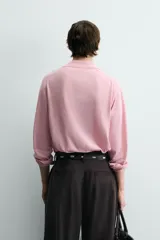 Polo de punto ligero color rosado, con cuello solapa, abertura frontal en V y manga larga.