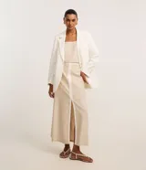 Pollera midi evasé color beige, confeccionada en mezcla de viscosa, algodón y lino, con cintura sastre, cierre lateral por cremallera y bies contrastante en tono claro a lo largo de la abertura frontal.