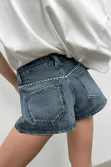 Shorts de jean tiro medio con bolsillos delanteros de plastrón decorados con tachas metálicas. Presenta cierre frontal con cremallera y botón metálico.