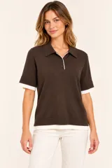 Remera polo de punto color marrón chocolate, con mangas cortas, cuello solapa y cierre frontal de botones. Cuenta con detalles en color blanco en el cuello, los puños y el ruedo, simulando un efecto de capas.