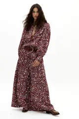 Pantalón de lino color bordó con estampado floral de margaritas en blanco, azul y naranja. Diseño de pierna ancha, tiro medio-alto con tablas delanteras, elástico en la parte trasera y bolsillos laterales.