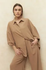 Camisa color beige de corte holgado, con cuello clásico, cierre frontal con botones a tono y mangas 3/4 con puños anchos.