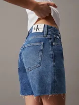 Short de jean estilo mom, de talle alto y lavado azul medio. Presenta un diseño clásico de cinco bolsillos, bragueta con cremallera y bajo con terminación deshilachada.