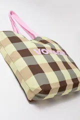 Tote bag de tela con diseño a cuadros en tonos marrón, beige y verde, tiras de hombro color rosado y la palabra "VOYAGE" estampada en el frente en color rosado.