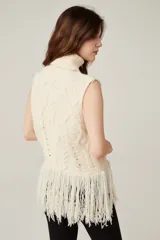 Chaleco de punto sin mangas con cuello polera, diseño de trenzas y rombos en relieve, y detalle de flecos largos en el ruedo.
