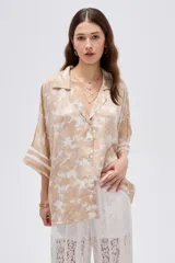 Camisa de poliéster holgada con estampado de paisaje en tonos beige y blanco, cuello solapa, cierre frontal de botones y mangas tres cuartos con puños anchos listados.