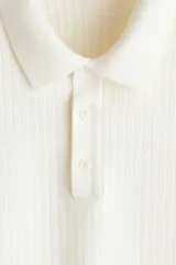 Remera polo de manga corta de H&M en punto texturizado color blanco, con cuello clásico, tapeta con botones y ribetes acanalados en puños y bajo.