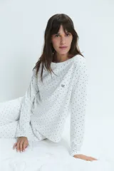 Pijama de dos piezas compuesto por remera de manga larga y pantalón, confeccionado en algodón blanco con estampado de lunares negros. La remera presenta cuello redondo y un pequeño bordado de corazones en el pecho.