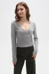 Sweater de punto gris con cuello en V, diseño cruzado y cierre lateral con botones. Presenta mangas largas y un ajuste al cuerpo con detalle acanalado en la cintura.