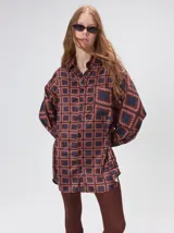Camisa de seda con cuello camisero, manga larga y bolsillo frontal. Presenta un diseño estampado geométrico de cuadrados en tonos marrones y azul oscuro.
