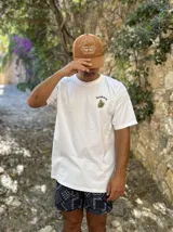 Remera blanca de algodón con cuello redondo y estampado en la espalda con imágenes de cogollos de marihuana y texto "BROKERS HIGH QUALITY GOODS".