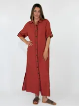Vestido largo de lino marrón con cierre frontal de botones, cuello camisero, mangas tres cuartos con presilla y costuras decorativas blancas en la botonera.