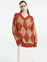Sweater de punto con escote en V y diseño de rombos en tonos marrón y naranja. Presenta un corte holgado, mangas largas con puños acanalados y terminación de ruedo también acanalada.